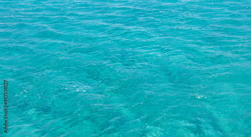 Sea surface blue turquoise color background, some reflections. Calm crystal clear water with small ripples.