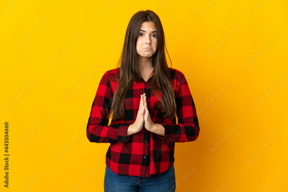 Teenager Brazilian girl isolated on yellow background keeps palm together. Person asks for something Teenager Brazilian girl isolated on yellow background keeps palm together. Person asks for something