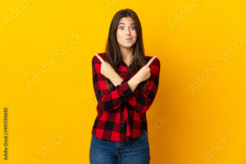 Teenager Brazilian girl isolated on yellow background pointing to the laterals having doubts © luismolinero
