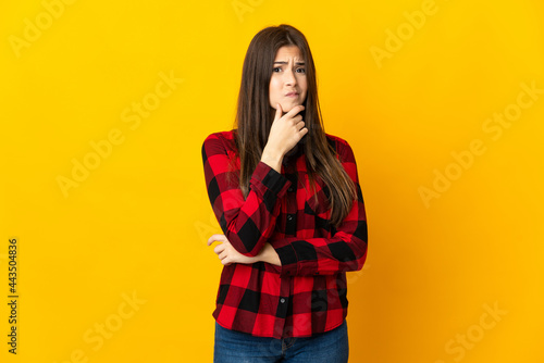 Teenager Brazilian girl isolated on yellow background having doubts © luismolinero