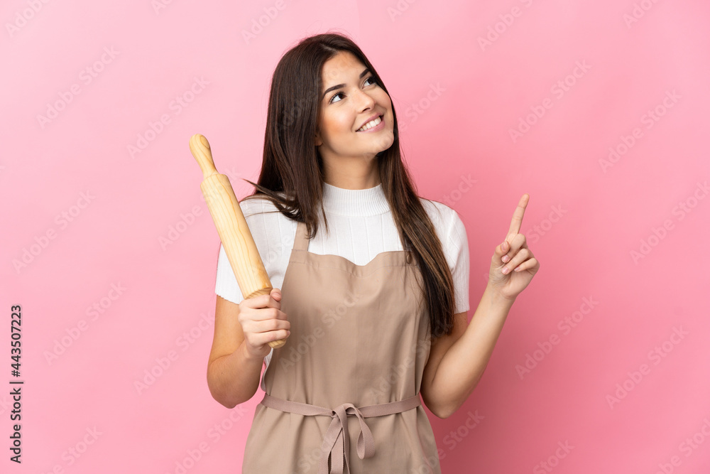 Teenager Brazilian girl holding a rolling pin isolated on pink background pointing up a great idea Teenager Brazilian girl holding a rolling pin isolated on pink background pointing up a great idea