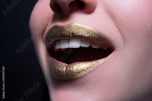 Smiling lips. Closeup sexy beautiful female golden lips isolated. Gold lipstick.