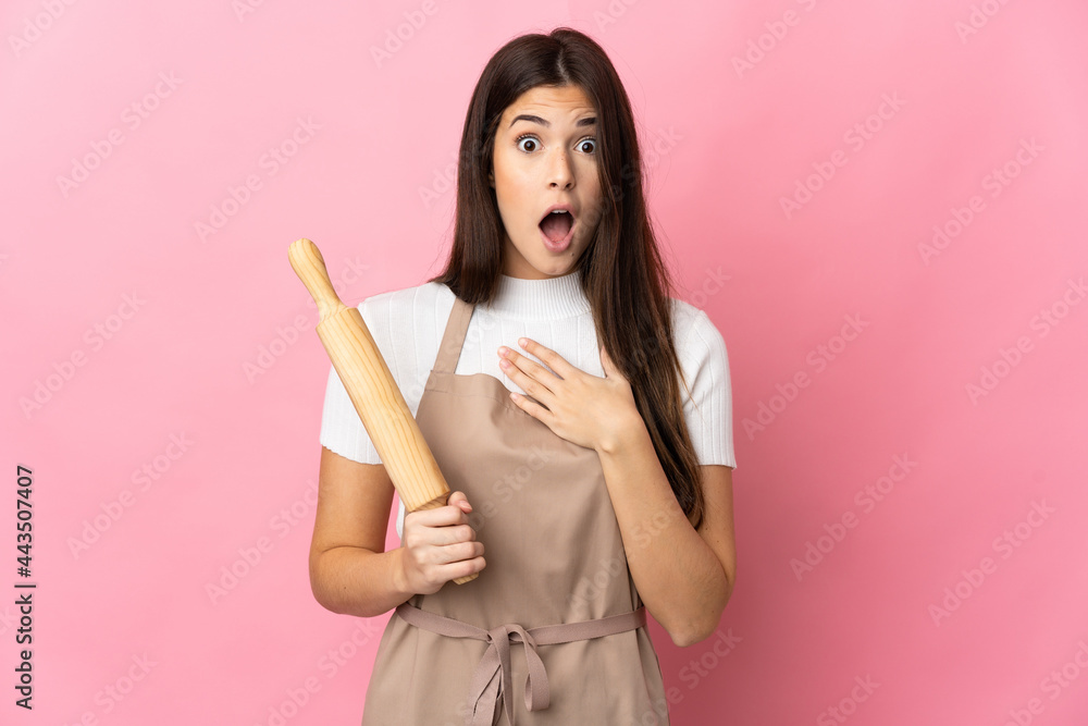 Teenager Brazilian girl holding a rolling pin isolated on pink background surprised and shocked while looking right Teenager Brazilian girl holding a rolling pin isolated on pink background surprised and shocked while looking right