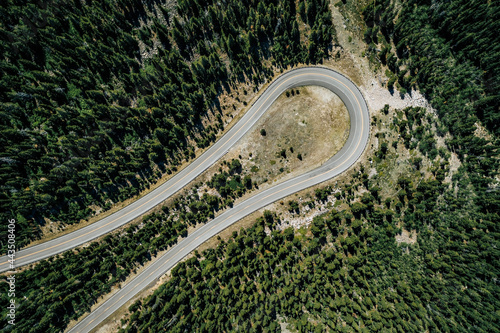Aerial top down view of cars on curve high mountain asphalt road among green trees, sunny day. Light effect applied