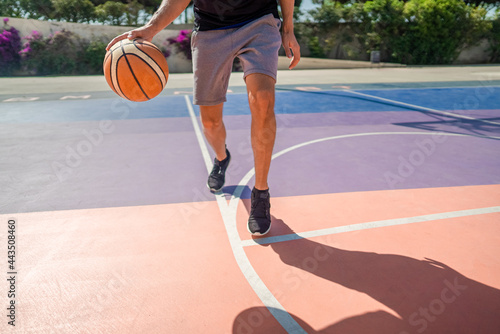 Legs of a professional basketball player dribbling the ball on the basketball field. The game is in full swing