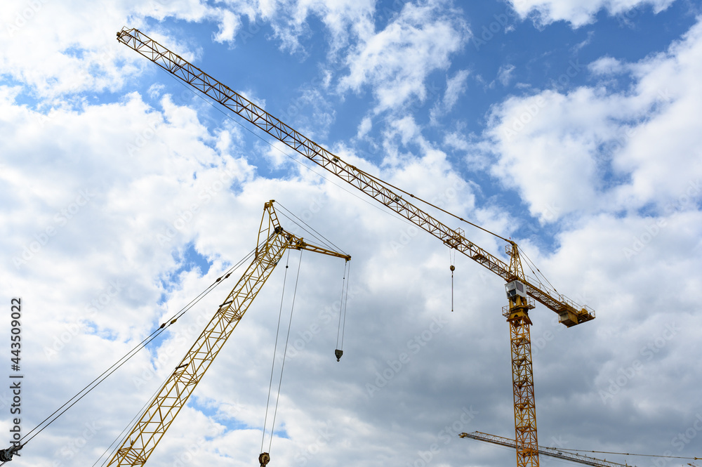 Construction cranes against the background of a blue sky with clouds. Construction cranes against the background of a blue sky with clouds.