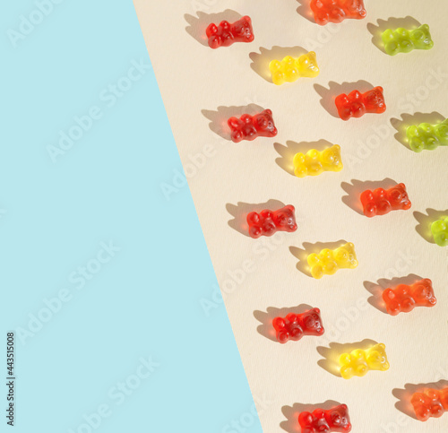 Creative pattern made with colorful gummy bears against the beige and pastel blue background. Summer flat lay.