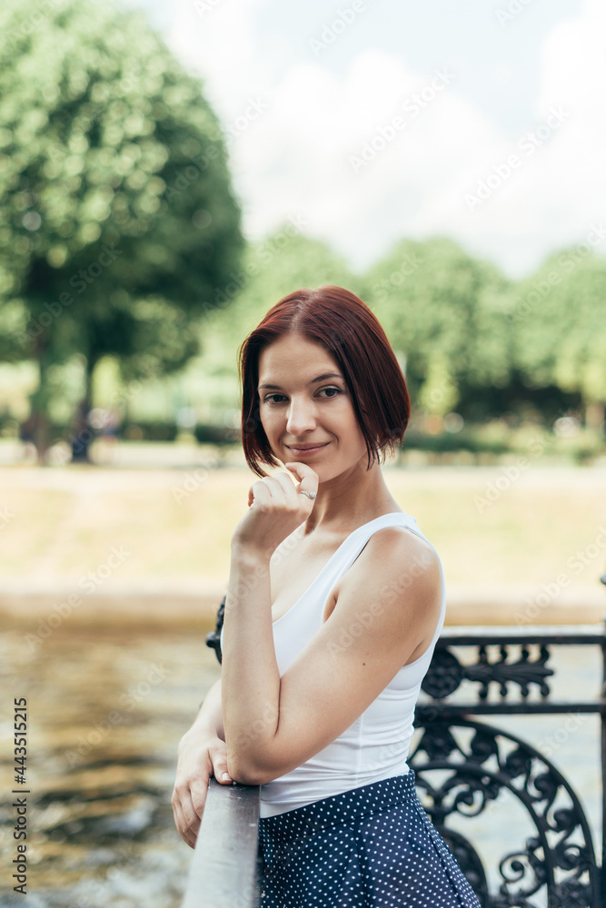 A girl with a bob hairstyle Caucasian walks in a city park on the bridge and looks at the camera