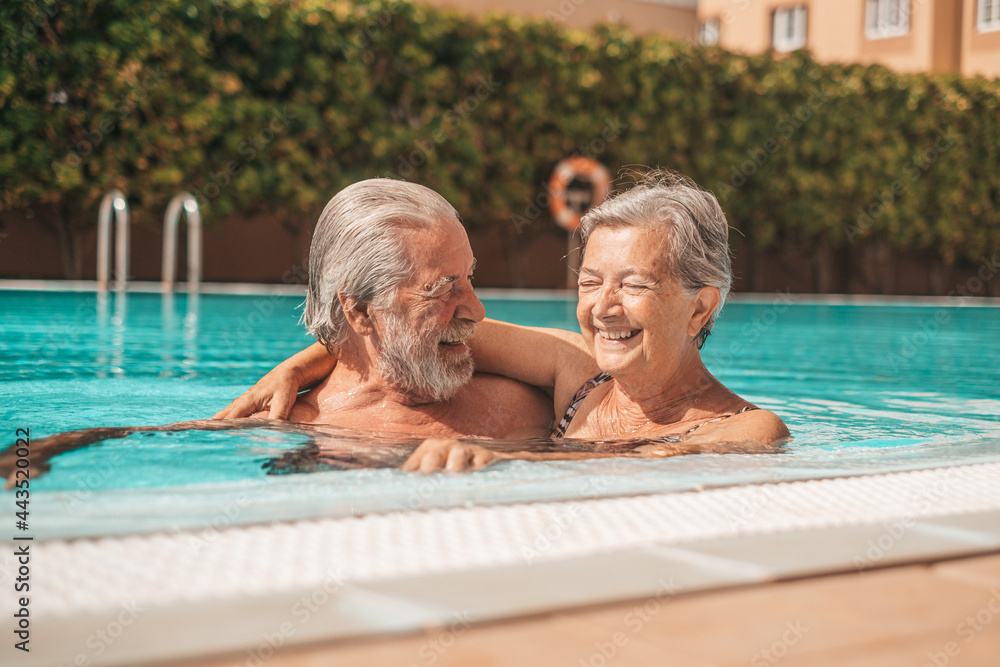 Couple of two happy seniors having fun and enjoying together in the swimming pool smiling and playing. Happy people enjoying summer outdoor in the water
