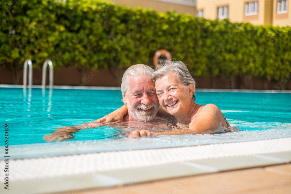 Fototapeta premium Couple of two happy seniors having fun and enjoying together in the swimming pool smiling and playing. Happy people enjoying summer outdoor in the water 