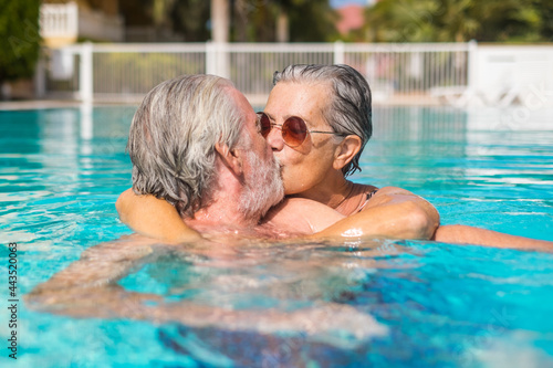 Couple of two happy seniors having fun and enjoying together in the swimming pool smiling and playing. Happy people enjoying summer outdoor in the water. © Daniel