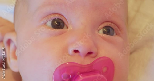 portrait of a small cute funny child who lies in his bed with a pink pacifier in his mouth and looks up in surprise.closeup. photo