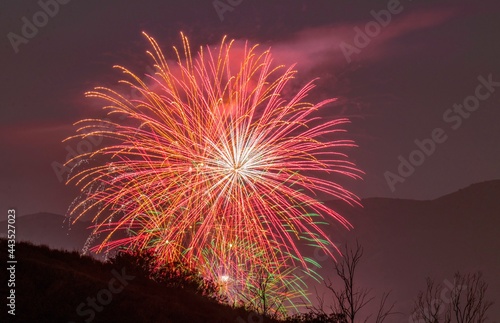This photograph captures a grand finale display of multiple aerial fireworks all exploding at once  illuminating a night sky behind a remote mountainous landscape. 