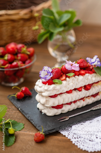 Pavlova dessert with strawberries and violet flowers as a decor on a wooden background