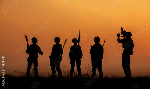 The military silhouettes of soldiers hold gun against with sunset sky background