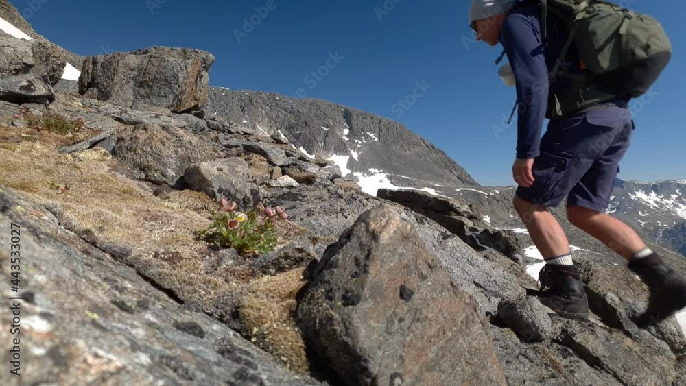 Hiker with backpack climbs steep terrain near a mountain top in Norway Hiker with backpack climbs steep terrain near a mountain top in Norway