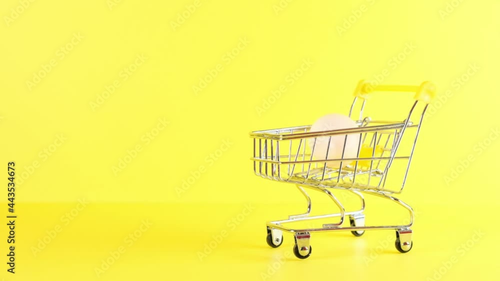 Shopping cart with eggs inside on a yellow background, closeup. Black Friday Shopping and Discount Concept. Shopping cart with eggs inside on a yellow background, closeup. Black Friday Shopping and Discount Concept.