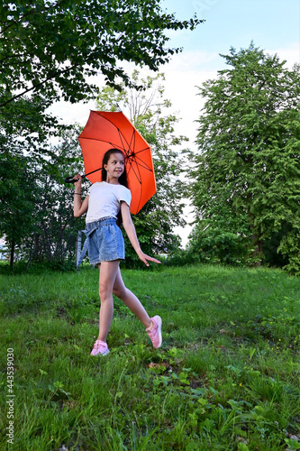 beautiful happy young girl with an orange umbrella is having fun on sunny summer day outdoors in park, dressed in white T-shirt and denim shorts. Travel, recreation, healthy lifestyle © IULIIA GUSEVA