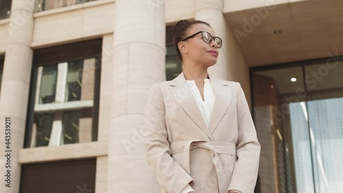 Wallpaper Mural Low-angle arc shot with slowmo of successful young Mixed-race businesswoman in smart casual beige suit and purse walking out of modern office building after work Torontodigital.ca