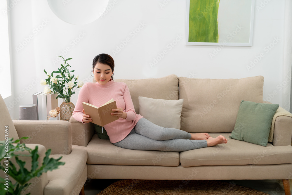 Beautiful smiling woman reading a book and lying on the sofa in the living room Beautiful smiling woman reading a book and lying on the sofa in the living room