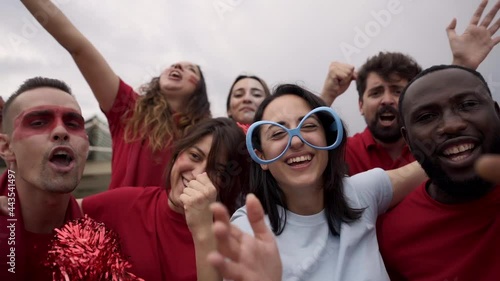 Group of supporters of a soccer team watching a game in the stands. Men and women euphorically celebrate a goal looking at camera. Group of different races support their team. photo