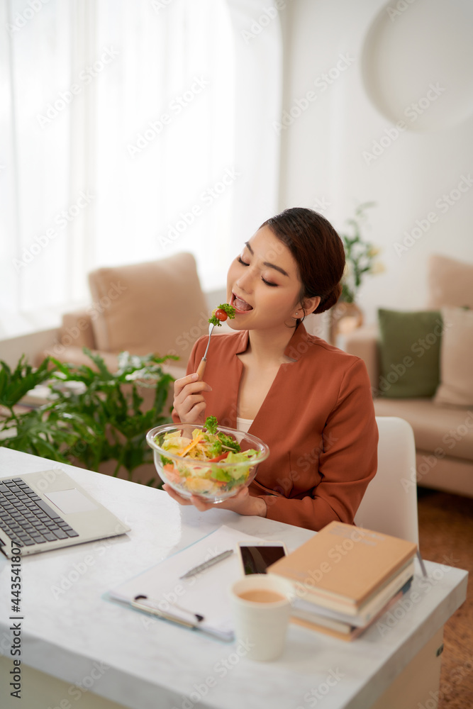 Portrait of woman watching movie on laptop and eating vegetable salad at table in breaktime