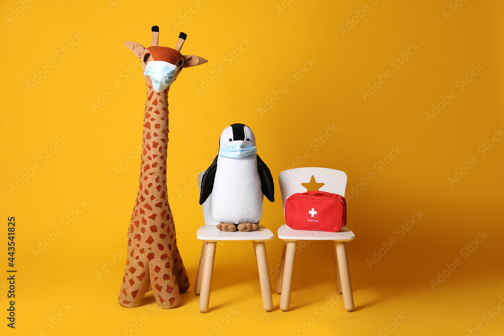 Obraz premium Toys with face masks and first aid bag on yellow background. Pediatrician practice