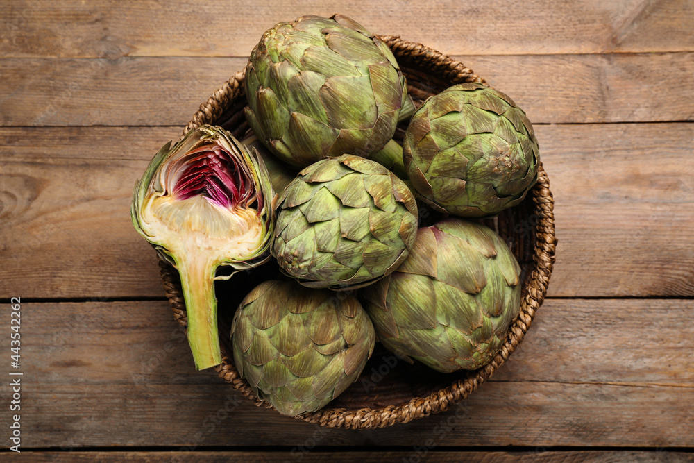 Cut and whole fresh raw artichokes in basket on wooden table, top view Cut and whole fresh raw artichokes in basket on wooden table, top view
