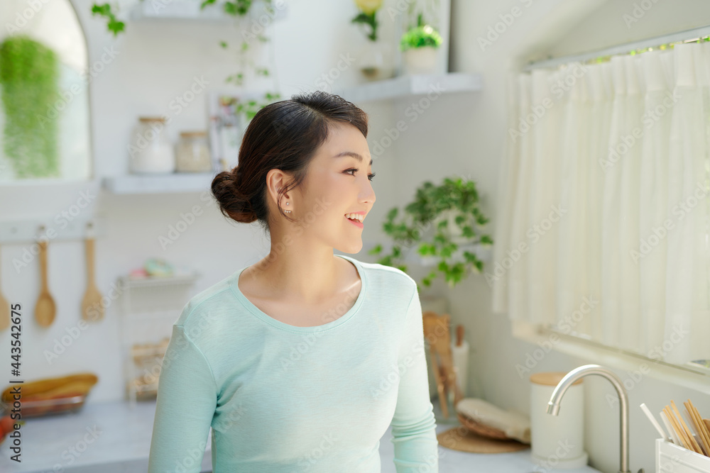 Happy asian woman drinking milk and looking away while standing in kitchen Happy asian woman drinking milk and looking away while standing in kitchen