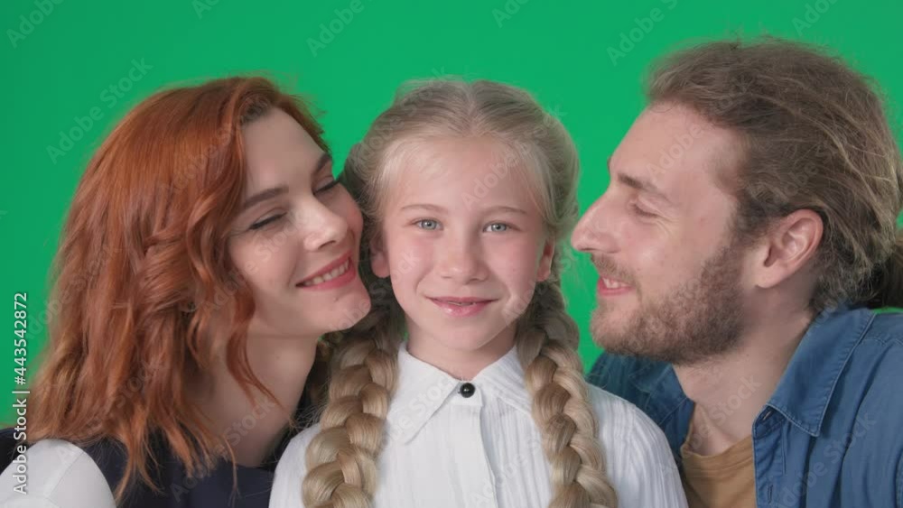 friendly family, loving mom and dad kiss on cheek beautiful daughter smile and look at camera on green background, chrome key friendly family, loving mom and dad kiss on cheek beautiful daughter smile and look at camera on green background, chrome key