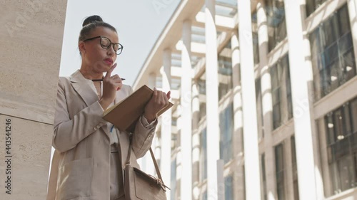 Wallpaper Mural Low-angle medium wide shot with slowmo of successful pensive young business lady taking notes in her notebook standing against column in city downtown Torontodigital.ca