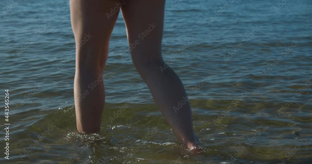 Close up white woman legs entering water at the beach Close up white woman legs entering water at the beach