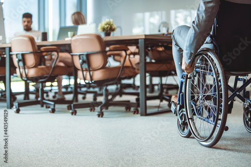 Cropped shot of disabled businessman in wheelchair. Businessman in wheelchair, hand on wheel close up, office interior on background. A man on a wheelchair Recovery