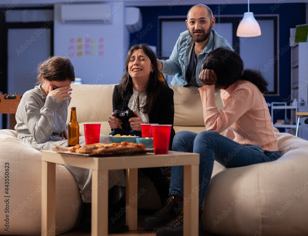 Diverse group of mates bonding while playing video game on tv console losing with joystick controller after work. Multi ethnic team enjoy office celebration party with snacks and drinks Diverse group of mates bonding while playing video game on tv console losing with joystick controller after work. Multi ethnic team enjoy office celebration party with snacks and drinks