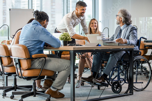 Group of business people in a meeting with colleague in a wheelchair for inclusion. Young businessman greeting handicapped business partner and team. Coworker on wheelchair photo