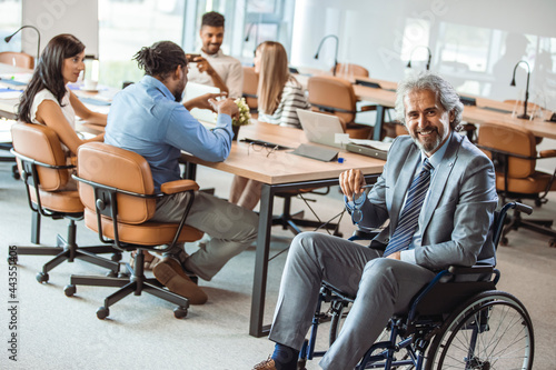 Portrait of smiling disabled business executive in wheelchair at meeting. Paralyzed man in a wheelchair. Shot of a team of businesspeople having a meeting in a modern office.