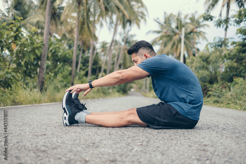 young man stretching in the park before running. Young man workout before fitness training at the park. Healthy and exercise young man warming up on the road in the forest. © Charnchai saeheng