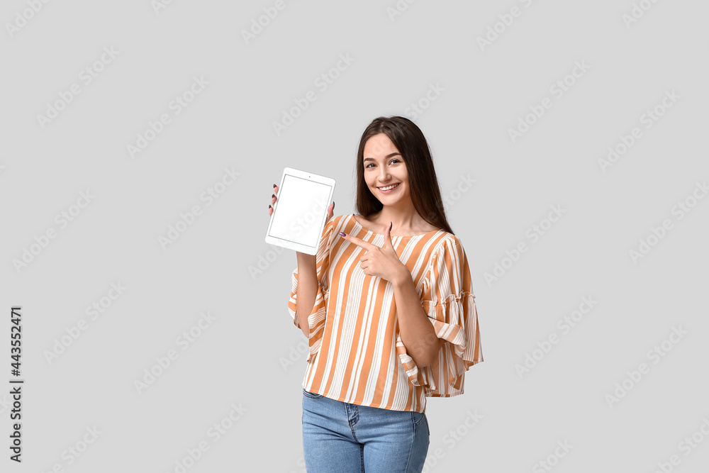 Young woman pointing at tablet computer on light background Young woman pointing at tablet computer on light background