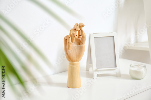 Wooden hand and blank frame on shelf near white wall photo