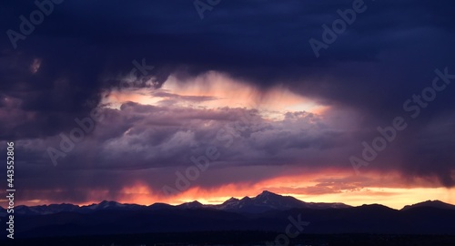 dramatic sunset and virga clouds over long's peak and the front range of the colorado rocky mountains, as seen from broomfield, colorado