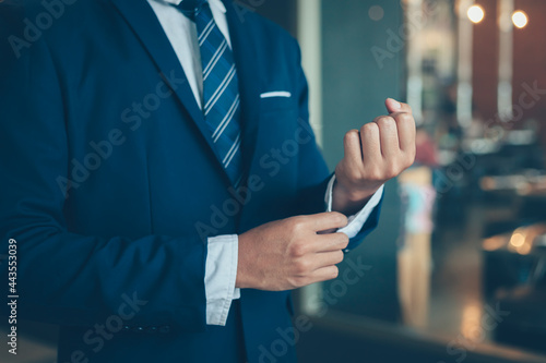 Billede på lærred businessman wearing business suit fasten cufflink or button on sleeve of classic jacket and factory background