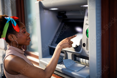 Beautiful african women using ATM machine. Attractive young woman withdrawing money from credit card at ATM.