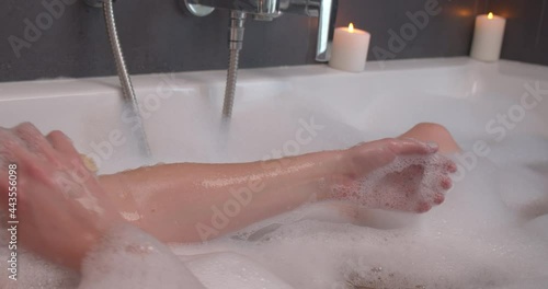 Woman arms stick up out of a bubble bath with candles and an exfoliating glove photo