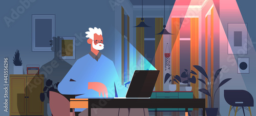 overworked senior man freelancer looking at laptop screen aged man sitting at workplace in dark night home room