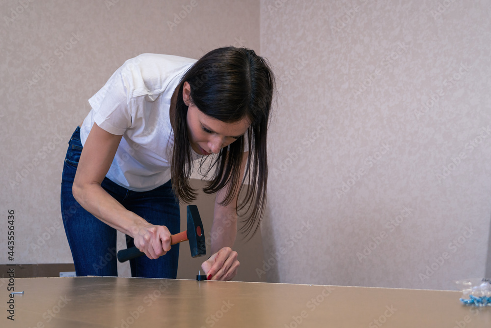 Self-Assembly furniture. Woman drives into the LDF by metal nail Self-Assembly furniture. Woman drives into the LDF by metal nail
