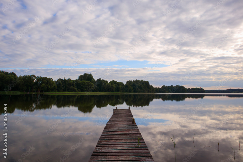 Fototapeta premium Wooden footbridge on the shore of the lake. Thick clouds above the lake