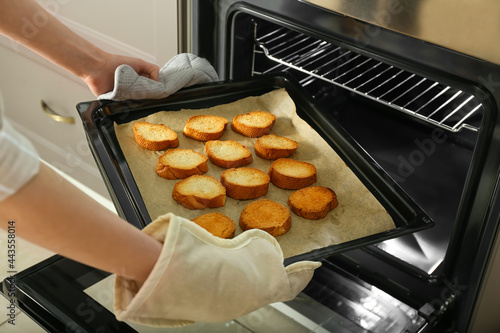 Woman taking baking sheet with toasted bread out of oven, closeup