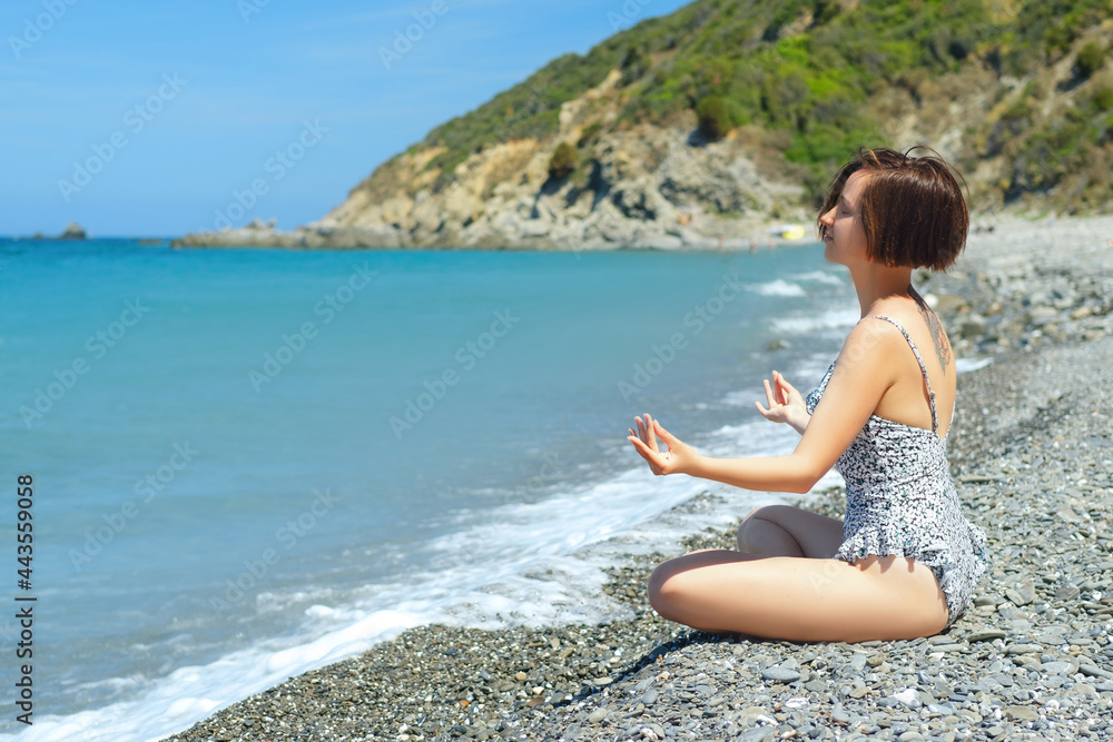 Caucasian female in swimsuit with tattoo doing Breathing Pranayama Exercise. Outdoor workout on the sea. Mindfulness zen spiritual meditation tips. Kundalini yoga. Reiki meditation. Unity with nature.