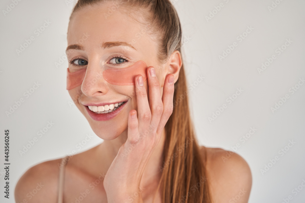 Woman wearing under eye patches touching her skin with satisfaction