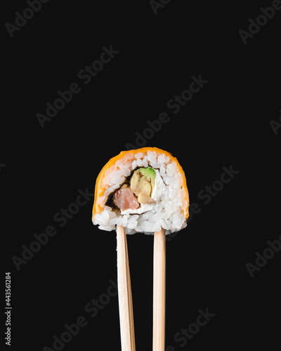 Hand holding sushi roll using chopsticks on black background. Cheddar cheese sushi roll over black